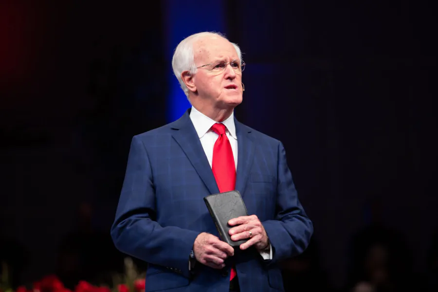 Pastor Bill Monroe preaching in a blue suit while holding his Bible