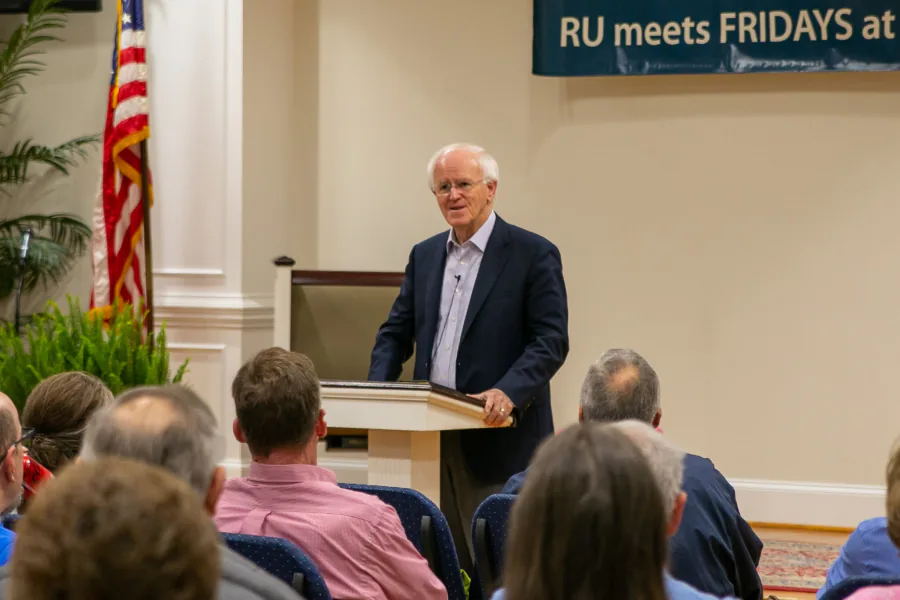 Pastor Bill Monroe speaking from a lectern at a Reformers Unanimous gathering